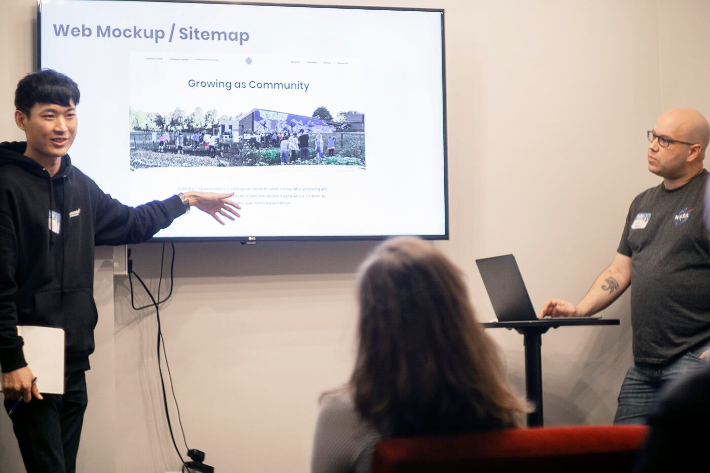 Two team members show website mockups presented on a TV to a small audience.