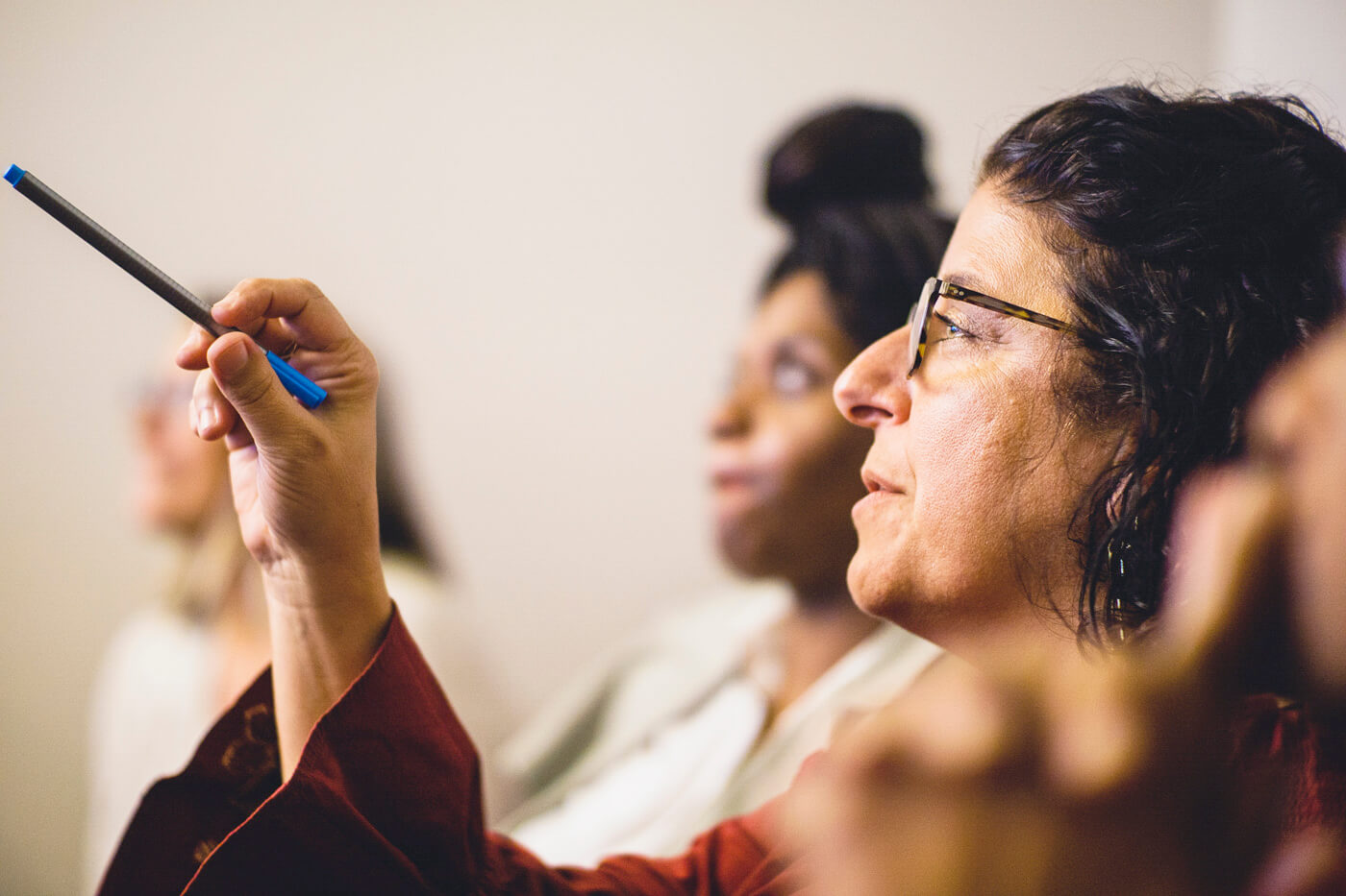 A woman gestures with a pen while speaking.