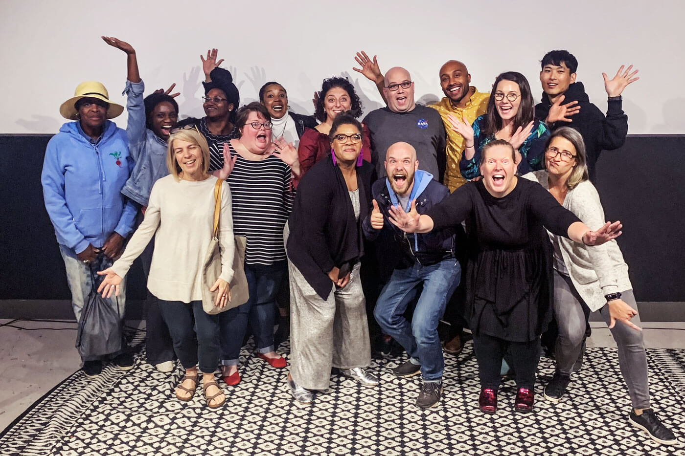 A group of 15 people pose together with smiles and their hands in the air.